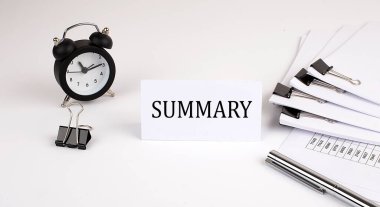 Ofis malzemeleri ve alarm saatinin yanında beyaz bir arkaplanda SUMMARY yazılı kart. İş dünyası