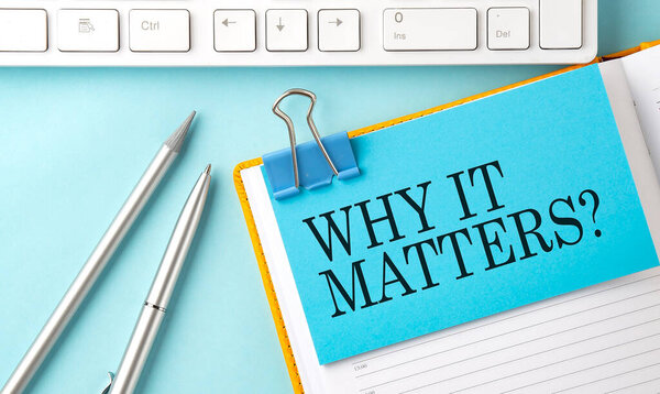 WHY IT MATTERS text on sticker on blue background with pen and keyboard