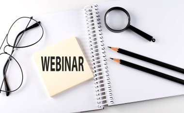 Kalemler, büyüteçler ve gözlüklerle defterin üzerinde WeBINAR kelimesi var.