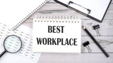 Masaüstünde kalem, ofis araçları ve grafiklerle en iyi çalışma yeri metni olan not defteri.