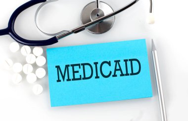 Steteskop, hap, kalem, tıbbi konsept içeren bir masaya MEDICAID metni yaz.