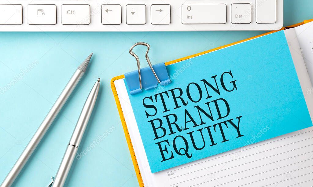 STRONG BRAND EQUITY text on sticker on blue background with pen and keyboard