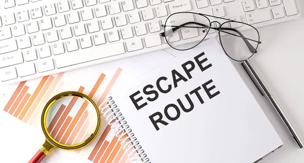 ESCAPE ROUTE text written on notebook with keyboard, chart,and glasses