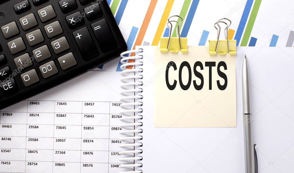 COSTS text, written on a sticker with calculator,pen on chart background.