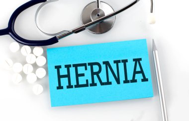 Steteskoplu, haplı, kalemli, tıbbi konseptli bir masada HerNIA mesajı..