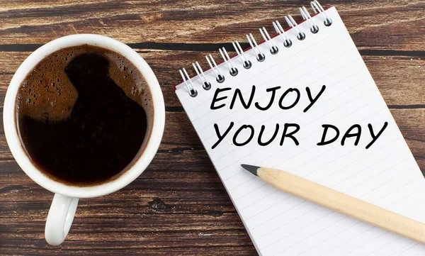 ENJOY YOUR DAY text on the notebook with coffee on wooden background