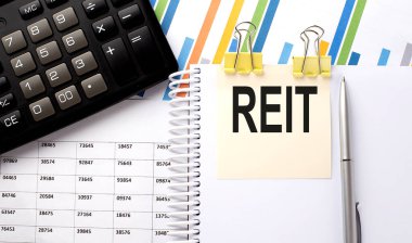 Hesap makineli bir çıkartma üzerine yazılmış REIT metni, grafik arkaplanındaki kalem.
