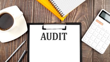 Kahve, hesap makinesi ve defterle kağıda yazılmış AUDIT metni. İş dünyası