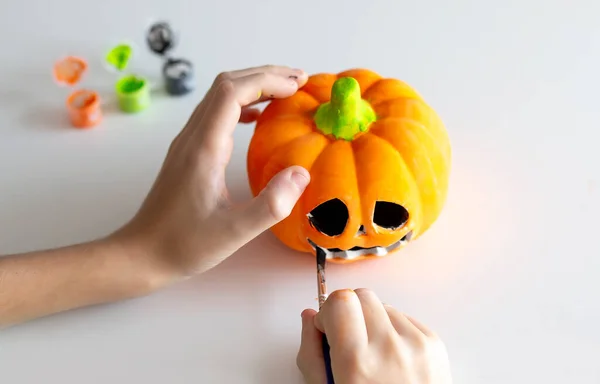 Child paints a pumpkin for Halloween on the white background