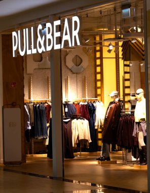 Bialystok, Polonya, 08.10.2025. Aydınlatılmış bir tabelayla Çek ve Ayı moda mağazası, raflarda moda giysiler ve sıcak tonlu iç mekanlarda mankenler.. 