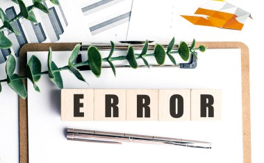 Kalem, yeşil yaprak ve finansal dökümanların bulunduğu beyaz bir panoda kelime hatası içeren tahta bloklar hata veya sorun olduğunu gösteriyor .