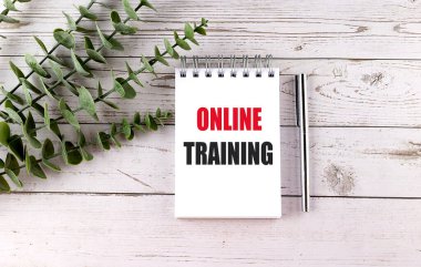 Tahta bir masanın üzerinde, uzaktan eğitimi veya dijital eğitimi temsil eden kalem ve bitkilerle çevrimiçi eğitim metni bulunan defter. .