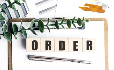 Tahta bloklar, finansal tabloları, beyaz zemin üzerinde kalem ve yeşil yapraklar olan bir pano üzerinde metin siparişi ile . 