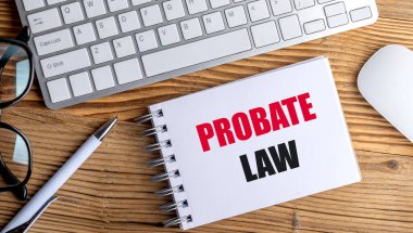 Tahta masa arkasında kalem, klavye ve gözlüklü spiral defter üzerine vasiyet metni. 