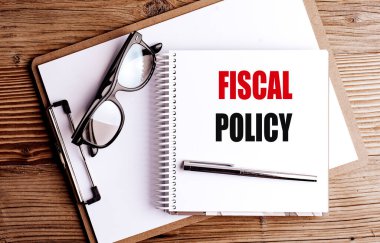 Not defterindeki mali politika cümlesi. Tahta arka planda pano, kalem ve gözlük var. . 