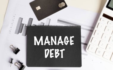 Hesap makinesi, kredi kartı ve ofis malzemeleriyle mali belgelerin borçlarını yöneten siyah kağıt.