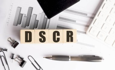 Tahta blokta, çizelgeler, hesap makinesi, kalem ve ofis malzemeleriyle DSCR kısaltması.. 