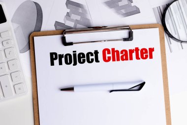 Ofis masasında kalem, büyüteç, çizelge ve hesap makinesi olan beyaz kağıt üzerinde proje tüzüğü metni.