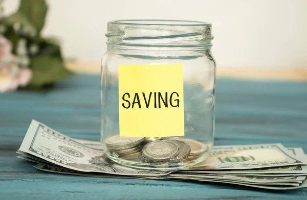 Glass jar with money and label save on table against blurred background. Space for text