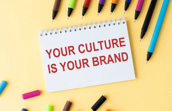 Your culture is your brand - handwriting on a notepad on yellow table with a colored pencils.