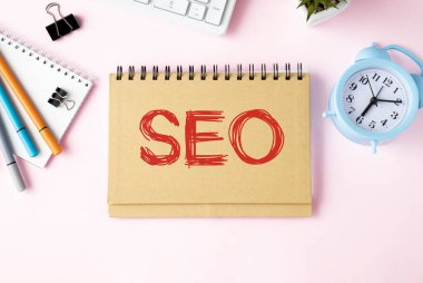 SEO içinde metin olan defter kahve, dizüstü bilgisayar ve buruşuk kağıtlarla dolu bir masada.