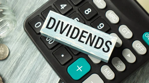 Text DIVIDENDS on wooden block with on a calculator , finance concept.