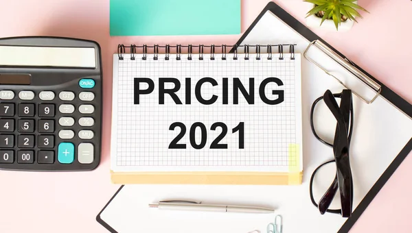 pricing 2021 is written on a Notepad that lies on the financial documents next to the calculator and cash in the form of dollars and coins. Business and financial concept