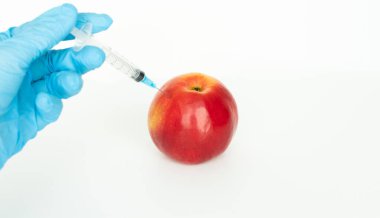 Beyaz tıbbi önlüklü ve mavi sterilize ameliyat eldivenli kadın doktordan güzel elmaya plastik şırınga enjekte edilmesini istiyorum.