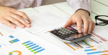 Hesap makineli bir iş adamı ofiste notlar alırken bir deftere yazar.