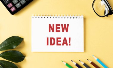 Sarı zemin üzerinde NEW IDEA yazılı not, bardakların ve ofis malzemelerinin yanında..