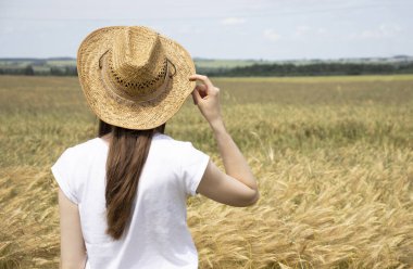 İnce yapılı bir kadının kollarını kaldırması, bir elinde hasır bir şapkayla buğday tarlasının ortasında zevkle ayakta durması, kırsal alanda yaz tatillerinin tadını çıkarması..