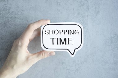 Elinde alışveriş saati yazılı bir kart tutuyor.