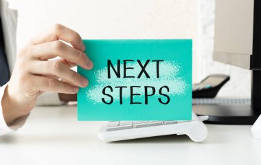 İş adamının elinde NEXT STEPS yazılı bir kart tutmasına yakın plan, yumuşak odaklı arka planı olan iş konsepti resmi