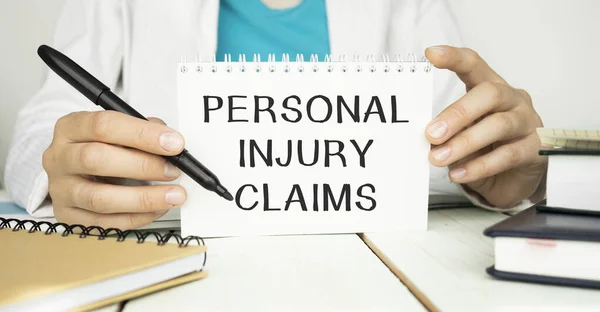 Word writing text Personal Injury Claims. Business concept for being hurt or injured inside work environment Man holding marker notebook clothespin hold reminder coffee cup wood table.