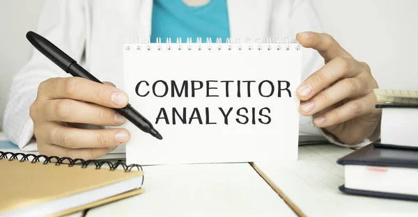 COMPETITOR ANALYSIS. Inscription on a white sheet of notebook near a white pen and pieces of paper