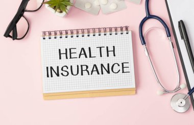 Ekranında yazılı metin sağlık sigortası olan bir tablet bilgisayar ve çizelge ve çizelge dolu bir masada steteskop.