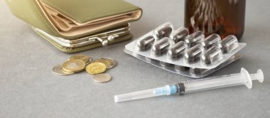 Tıbbi masraflar: Ahşap bir masanın üzerinde bozuk para ve haplar yığını, kısa odak, arka planda cüzdan