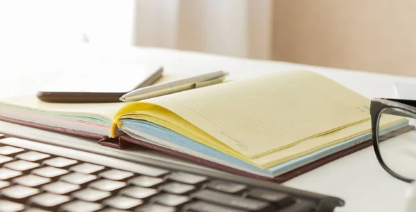 Open notebook, tablet computer, glasses and folders on the office table. Top view with copy space. Free space for text. Office workplace