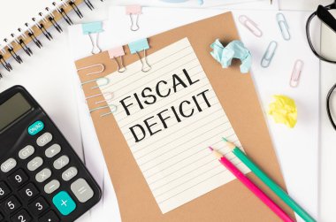 Notlar, hesap makinesi ve beyaz arkaplanda kum saati için FISCAL DEFICIT kağıdı yazılı beyaz kart. İş konsepti. Kahverengi arkaplan.