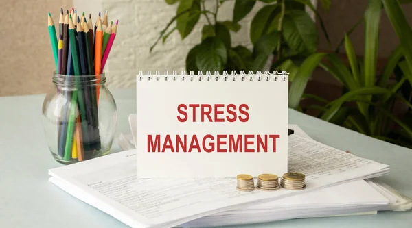 Stress Management statement on paper note pad. Office desk with electronic devices and computer, wood table from above, concept image for blog title or header image. Aged vintage color look.