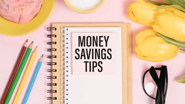Notebook with text MONEY SAVINGS TIPS near office supplies.