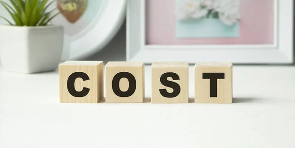 Cost, expense or company profit and loss concept, cube wooden block with alphabet combine word COST on white grid paper, analyze spending or payment.