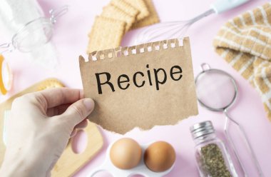 Kağıt üzerinde tarif metni, tahta kaşıklar ve beyaz pembe arka planda tahta.