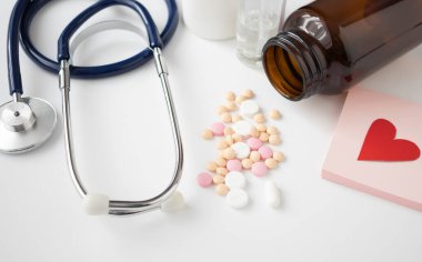 Tıbbi ekipman stetoskobu, termometre, kardiyogram ve haplar beyaz arka planda bir doktorun ofisinde..