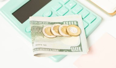 Dolar banknotları ve altın sikkeler, kapalı görüşlü gri ve beyaz düğmeli vintage hesap makinesinin yanında yatar.