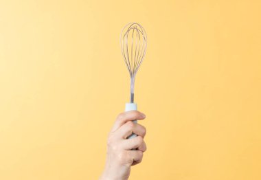 Sarı kağıtta metal bir çırpı tutan eller. Krem şanti veya yumurta çırpmak için mutfak aracı.