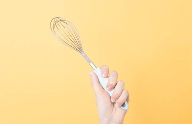 Sarı kağıtta metal bir çırpı tutan eller. Krem şanti veya yumurta çırpmak için mutfak aracı.