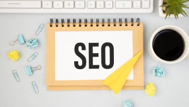 SEO içinde metin olan defter kahve, dizüstü bilgisayar ve buruşuk kağıtlarla dolu bir masada.