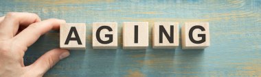 Yaşlanma kelimesi, kağıt bir arka planda steteskopun yanındaki tahta küplere yazılmıştır. Tıbbi konsept.
