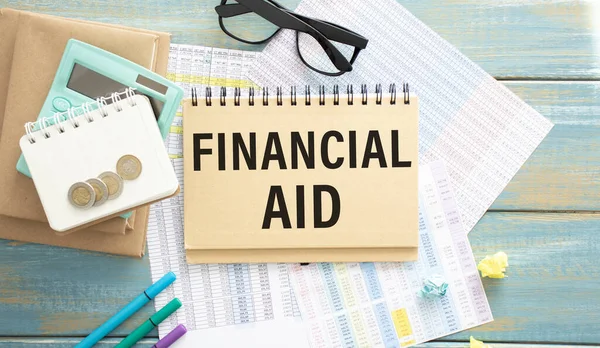 Financial Aid text written on a notebook with pencil, calculator and coins